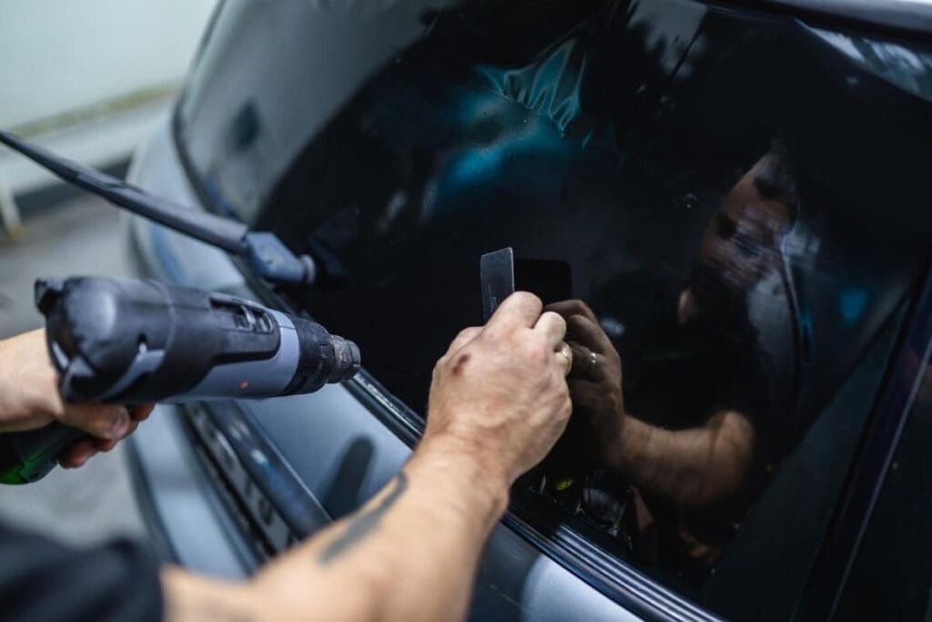 Technician fitting window tint film to a car door window with a heat gun